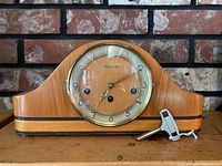 Front view of Forestville mantel clock on wooden surface, showing wood body with metal trim and attached metal winding key.