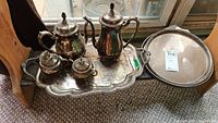 Full view of silver plate tea and coffee set arranged on ornate rectangular tray with an additional round tray beside it.