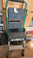 Featherlite step stool folded showing black textured platforms and green frame