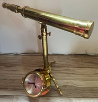 Side view of brass adjustable telescope mounted on a stand with brass ships bell clock at base.