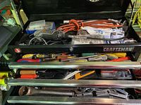 Overall view of Craftsman black metal toolbox filled with assorted hand tools, screwdrivers, wrenches, pliers, and power tool cords.