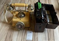 Both phones shown side by side on floor: cream rotary phone and metal WW2 field phone case opened with handset and cord visible.