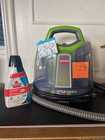 Bissell Little Green ProHeat Pet spot cleaner unit with handle, water tank, and hose, along with the cleaning solution bottle.