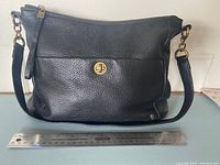 Front view of the black leather purse with brass turn-lock, showing approximate 12 inch width using a ruler.