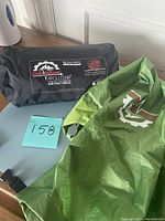 Photo showing compact black and gray blowup sack with Gear Doctors Apollo Air branding and text 'Big Boys Edition'. Green camping mat fabric is partly visible.