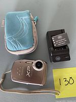 Silver Fujifilm FinePix XP10 camera, battery charger, rechargeable battery, and blue-gray padded carrying case on grey surface.