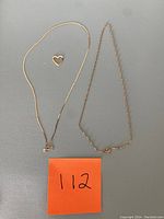Overview of two gold chains and heart pendant on gray background