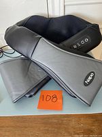 Front and side view of the Naipo neck and shoulder massager showing padded ergonomic design with control buttons and power adapter.