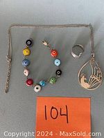 Image showing the evil eye bracelet, silver ring, and peacock pendant with chain laid out on a grey surface.