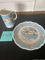 Photo showing the full plate and tall mug side by side, with the plate's scalloped edges and snowman carrying child design clearly visible.