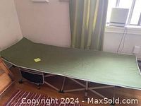 Full view of the unfolded green canvas camping cot with metal frame in a room, showing its size and structure.