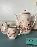 Full view of coffee pot, cream pitcher, and sugar bowl with floral design on countertop.