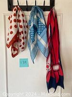 Three vintage scarves hanging on hooks against a white wall showing designs and colors