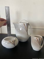 Photo shows three-piece porcelain tea/coffee set with hand holding ruler to measure size.