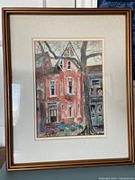Framed watercolor painting displayed on a wall showing urban buildings and a large tree.