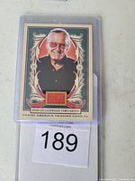 Front of the 2013 Panini Golden Age Stan Lee trading card featuring his portrait and fabric swatch with numbering 0249/999
