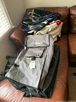 Multiple bags including a gray duffel bag with front flap on a brown leather couch along with black bags underneath.