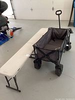 Full view showing the off-white folding bench beside the Quest wagon with large black wheels and black fabric body.