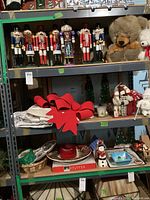Shelf showing seven nutcracker figures, plush animals, tree skirts with red bows, garland, and other assorted Christmas decor
