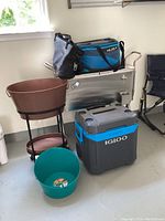 Full view of all items: Igloo cooler, brown plastic ice tub on stand, teal plastic ice tub, Ultra by Arctic Zone soft cooler, Trinity metal cooler on wheels.