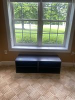 Dark brown storage bench positioned under a window on carpeted floor.