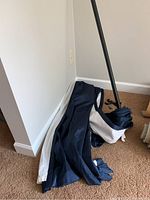 Navy blue blackout curtain fabric folded on carpet with curtain rod section and hardware pieces scattered