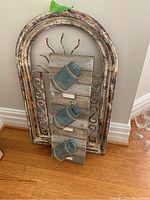 Photo showing the wood panel with three attached blue glass bottle vases in front of the arched metal panel.