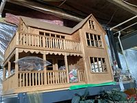 Photo of the full two-story wooden dollhouse showing exterior details and furniture bags inside visible through railings.