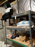 Shelf with large black gorilla plush in white shirt on top, assorted stuffed bears, blankets, and quilts on shelves below