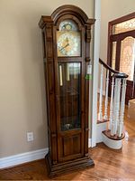 Front view of the wood grandfather clock showing clock face, glass door, pendulum, and wooden detailing.