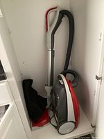 Full view of Kenmore canister vacuum with hose and aluminum wand stored in white cabinet.