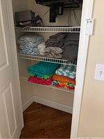 Photo of shelves showing stacked folded full and queen size sheet sets in gray, beige, light blue, and patterned versions on upper shelves.