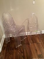 Five transparent Lucite chairs stacked together and one chair standing next to the stack on a hardwood floor.