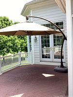 Full view of Sunbrella brown patio umbrella installed on deck with curved metal arm and base.