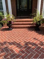 Wide shot of both black decorative outdoor planters placed on a brick porch next to steps, with colorful flowers planted inside them.