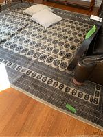 Full view of rectangular cream and black patterned area rug under furniture with two white pillows on it.