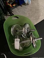 Top-down view of two assembled dumbbell bars with weight plates in green plastic container.