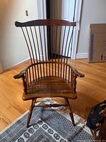 Front view of a wooden Windsor style chair showing the spindle back, armrests, and seat, placed on a patterned rug.