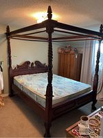 Full view of four poster bed with mattress showing carved posts and headboard against wall in bedroom.