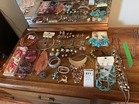 Wide angle photo showing costume jewelry including bracelets, earrings, necklaces, and brooches spread on wooden surface in front of mirror.