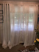 Sheer curtains with lace detailing and solid panels hung on curtain rod covering window. Curtains are white/off-white in color.