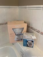 Conair True Glow facial sauna system and Life Premium blood pressure monitor in their original boxes on a tiled bathroom surface.