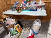 Wide view of white folding work table with metal legs, holding various craft supplies including flowers, glue, and boxed items.