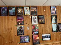 Wide view of all framed movie sheets on wooden wall paneling, showing 12 sheets in black frames including recognizable movies like Guardians of the Galaxy Vol. 2, Godzilla, Lion King, and others.