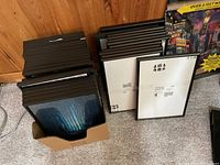 Multiple black Ikea 8x10 picture frames stacked and in box on carpeted floor against wood paneling.