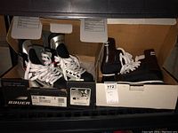 Photo showing two pairs of hockey skates inside open boxes on a shelf, focusing on the Bauer Vapor Pro Sr CTC pair in black, silver and white.