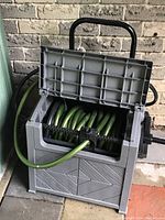 View of open gray plastic hose caddy with green hose visible inside, showing internal hose storage and crank mechanism.