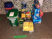 Overview of open and sealed containers of Finish dishwasher tabs, boxed Ziploc bags, sponges, and soap dispenser on kitchen counter with tiled backsplash
