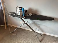 Ironing board fully assembled with iron rest and iron placed on top alongside spray can
