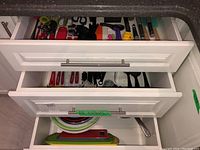 Three kitchen drawers opened showing various kitchen utensils, mixing bowls in one drawer, and cutting boards in another.